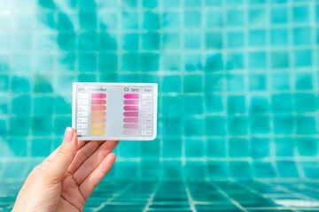 Water testing test kit in girl hand over blurred clear swimming pool water background, equipment...