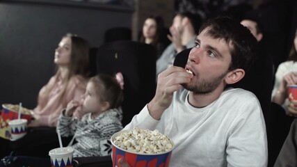 Dolly move of people are eating popcorn and watching a movie in the cinema