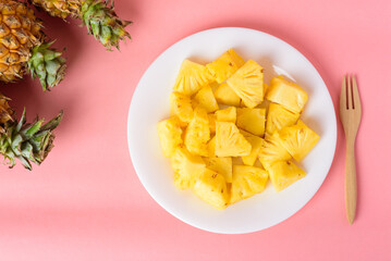 Sliced pineapple fruit on white plate with fork ready to eating on pastel pink background, Tropical fruit