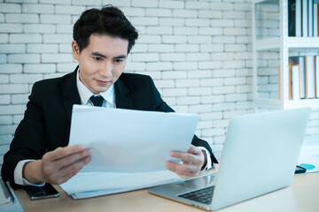 Happy of successful asian young businessman have stressed see a the document business plan and laptop computer on wooden table In the office room background.
