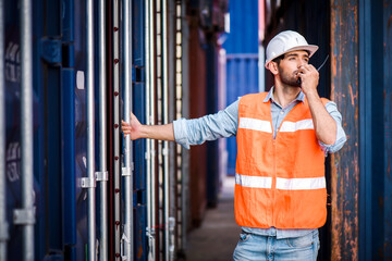 Confident Caucasian man engineer wearing white safety helmet using walkies talkie call to driver and check for control loading containers box from Cargo freight ship for import and export, transport