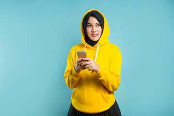 young indonesian women wearing yellow casual sporty hoodie sweater holding a cell phone while looking aside on isolated background