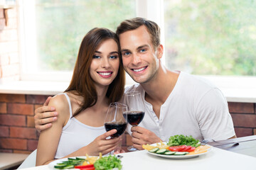 Beautiful smiling amorous couple drinking red wine, at home. Portrait image of caucasian models with redwine glasses in love concept. Happy man and woman together indoors.