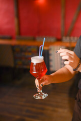 Woman hand holding cocktail in old fashioned glass with ice cubes and colorful straws. Beer cocktail in a bar.