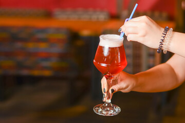 Woman hand holding cocktail in old fashioned glass with ice cubes and colorful straws. Beer cocktail in a bar.
