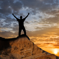 man silhouette with hands rising up stay on a mount top at the sunset, winner in a mountain