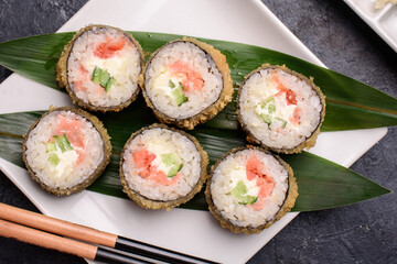 Set hot rolls with avacado, salmon, cream cheese, seaweed, soy sauce, ginger on a dark table.