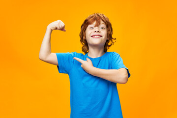  strong red-haired boy points to the muscles of his arms