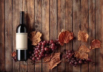 Bottle of red wine with ripe grapes and dried up vine leaves.