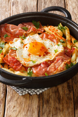 Spanish cuisine fried egg with fries and ham close-up in a plate. vertical