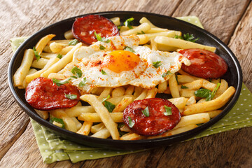 Spanish style fried egg with French fries and chorizo sausage close-up in a plate on the table. horizontal