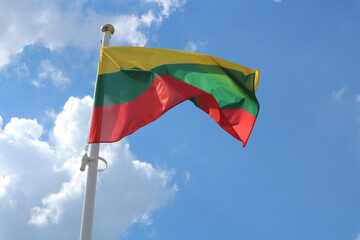 Lithuanian flag waving in the wind against a summer sky with white clouds.