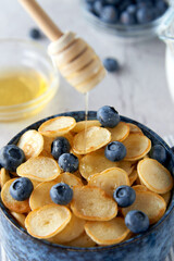 Blue Bowl of mini pancake cereal with blueberries, maple syrup and milk on concrete background. Tiny pancakes, new food trend concept. Cute healthy breakfast or snack. Recipe, menu.