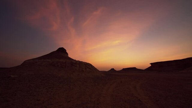 Time lapse of sunset in Zekreet Desert in Qatar with jebel hills and car tire tracks in the foreground.