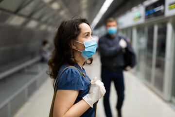 Portrait of female passenger in disposable face mask and latex gloves waiting for train on subway...