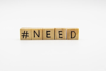 A word NEED with hashtag. Wooden small cubes with letters isolated on white background with copy space available. Concept image with hashtag.