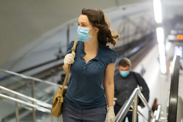 Focused young woman in disposable face mask and latex glove climbing stairs, leaving metro station. Concept of social distancing in context of coronavirus pandemic