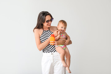 Mother and her little daughter with sunscreen cream on light background