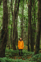 woman in yellow raincoat walking by rainy forest