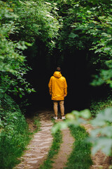 man in yellow raincoat sanding in front of dark entrance to the forest