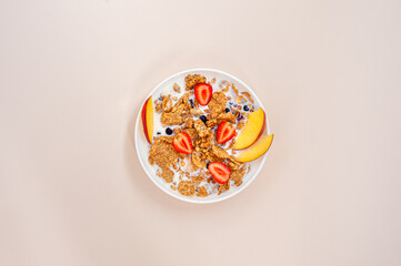 Light summer breakfast. Granola and wheat flakes with fruits, berries and milk on a light pink background. View from above.