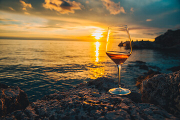 glass of wine at rocky sea beach on sunset