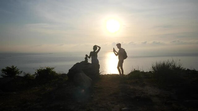 Unrecognizable couple taking pictures on a cliff viewpoint at sunrise.