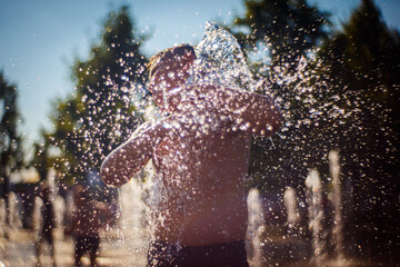 Fototapeta premium The boy bathes in the fountain. Water splashes in focus.