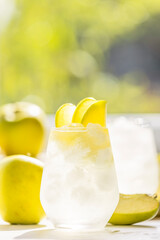Summer cocktail with green apple and ice on the white table near window in the sunny summertime. Selective focus image with copy space