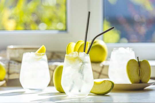 Summer cocktail with green apple and ice on the white table near window in the sunny summertime. Selective focus image with copy space