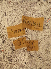 Pieces of brown paper reading 'Happy Birthday 2020' amidst paper shreddings 