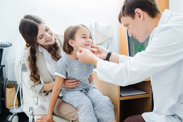 Social little girl in being examined by pediatrician, sitting on mom's lap