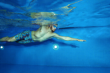 Young man swimming in the swimming pool shot from underwater