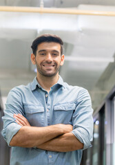 Cheerful young casual man standing with arms crossed in office