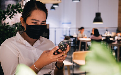 A young woman wearing face mask is traveling Coffee shop and use smartphone, New normal travel after covid-19 pandemic concept.