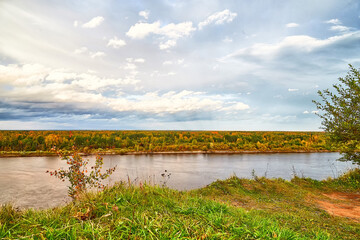 View on the river from top place on the bank through branch of trees and sky with clouds background. Nature landscape in an autumn day