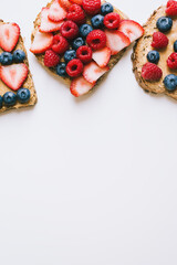 Vertical background with peanut butter toasts with seasonal berries. Brown bread with creamy spread, strawberry, blueberry and raspberry on white table. Healthy snack
