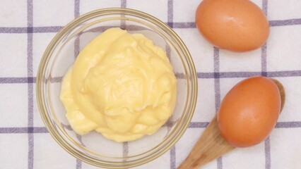 Homemade custard cream in a glass bowl with two fresh egg and a wooden spoon,on a table cloth top view