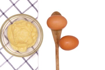 In selective focus homemade custard cream in a small bowl with two fresh eggs and blurred a wooden spoon,on white isolated background with copy space 