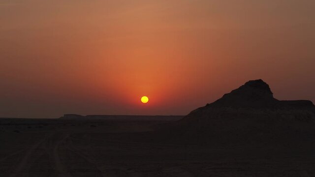 Wide shot of a sunset with rocky hills in the foreground in Zekreet Desert in Qatar.