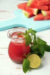 Glass jug with watermelon juice, lime, mint and watermelon slices on the white wooden Provence style table.