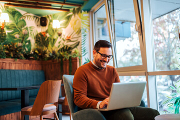 Smiling handsome man using laptop in cozy cafe.