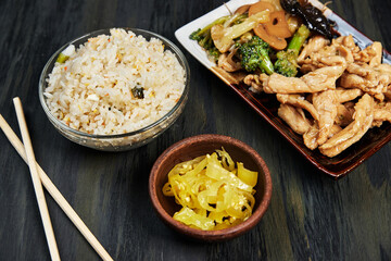 Chinese food served on an oriental plate with soy sauce, chilli and chopsticks on a dark wooden board