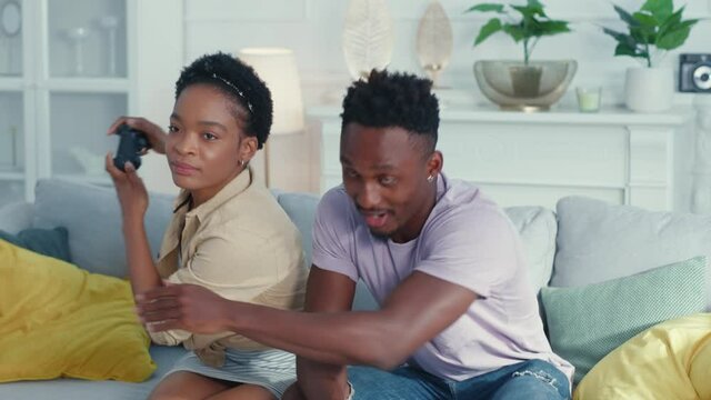 Attractive happy excited afro-american couple pplaying video game console with josticks bothering and competing with each other. Apartment. People.