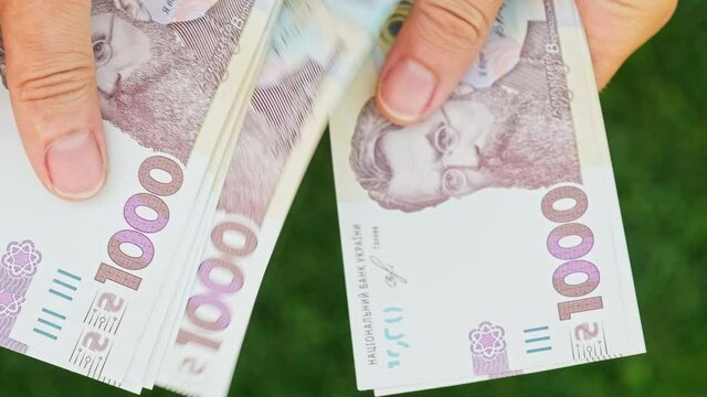 Cinematic shot: Men's hands consider Ukrainian money with a nominal value of one thousand hryvnias. Person counts banknotes. Man counts a large wad of money. Human hands with money