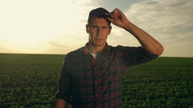 A farmer in a field at sunset. The face of a man outdoors on a crop farm looks at the camera. An employee, an agronomist adjusts his cap and hat. The concept of agribusiness.