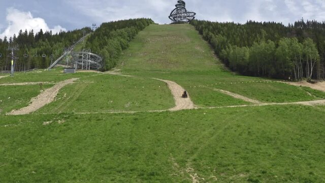 Tracking aerial 4k shot of a four wheeler driving up a green slope in the mountains of Dolní Morava, Czechia, heading towards The Sky Walk attraction between forests. Four wheeler driving uphill.