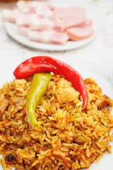 Eastern cuisine. Red plate with pilaf on the table. Sliced plate of brisket and sausage.