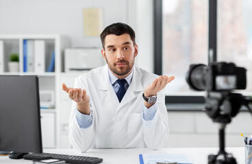 healthcare, medicine and blogging concept - male doctor with camera recording video blog at hospital