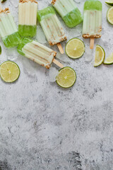 Fototapeta na wymiar Lime and cream homemade popsicles or ice creams placed with ice cubes on gray stone backdrop